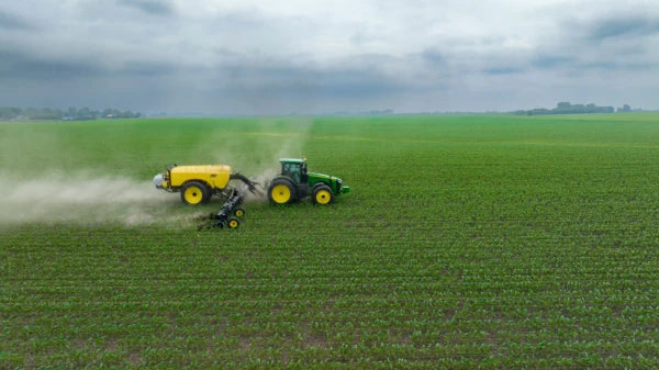 A tractor spraying a lush green field under a cloudy sky